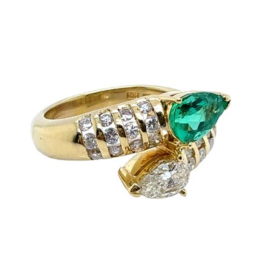 Lot 13 - An emerald and diamond set crossover ring. The...