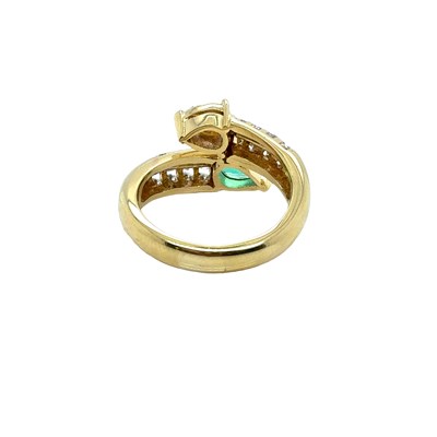 Lot 13 - An emerald and diamond set crossover ring. The...