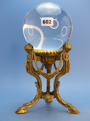 Lot 602 - A clear glass sphere supported on three brass...